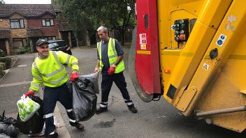 Photo of two waste collection crew members putting black rubbish bags in to a waste truck