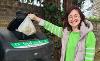 A woman dropping a bag of food waste in an outdoor food waste recycling bin.