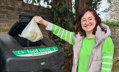A woman dropping a bag of food waste in an outdoor food waste recycling bin.