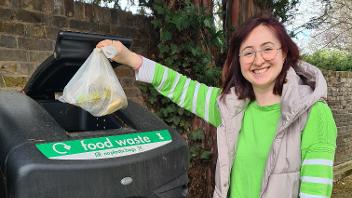 A woman dropping a bag of food waste in an outdoor food waste recycling bin.