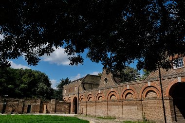 View of the brick facade of Cranford Park, from the shade of a hanging tree in the foreground and blue skies behind.