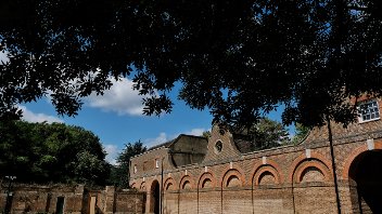 View of the brick facade of Cranford Park, from the shade of a hanging tree in the foreground and blue skies behind.