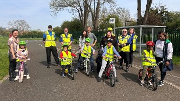 A group young children with their bikes and cycling instructors, wearing high-vis and helmets