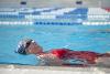 Older woman in red swimsuit doing swim exercises in swimming pool.